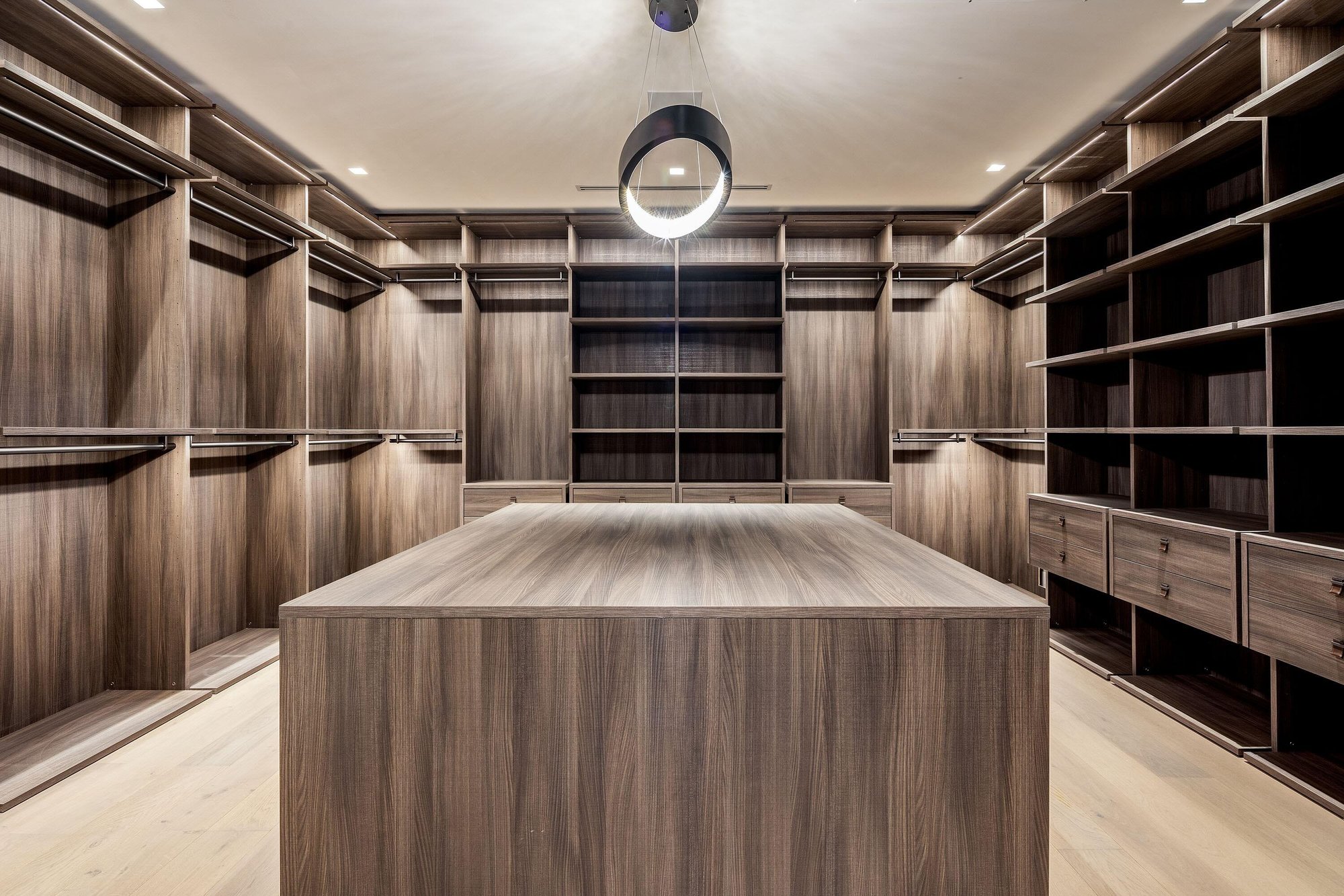 Spacious walk-in closet with wood grain island, open shelving, and modern halo chandelier.