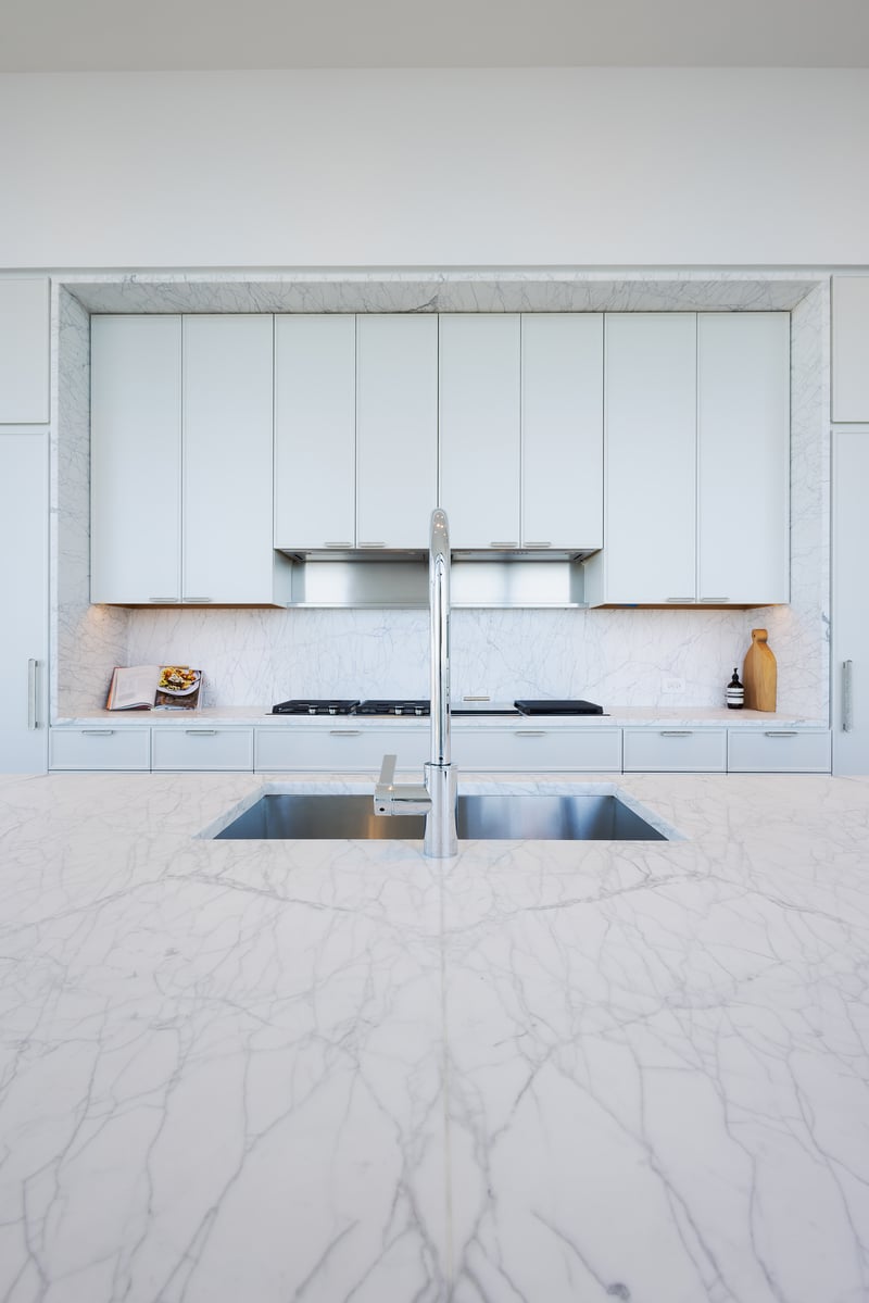 Minimalist kitchen with marble waterfall island, matching marble backsplash, and sleek white cabinetry.